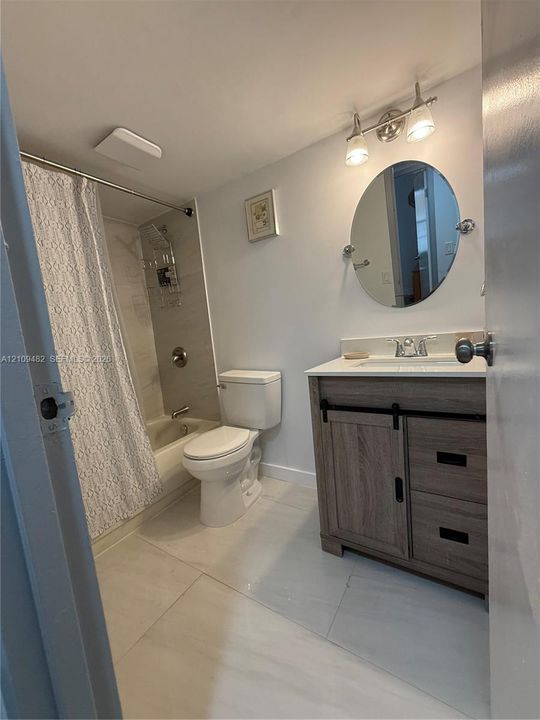 Bathroom featuring a wood-finish vanity with a stone-top integrated sink, oval wall-mounted mirror, brushed metal hardware, and a tub-shower combination with tile surround