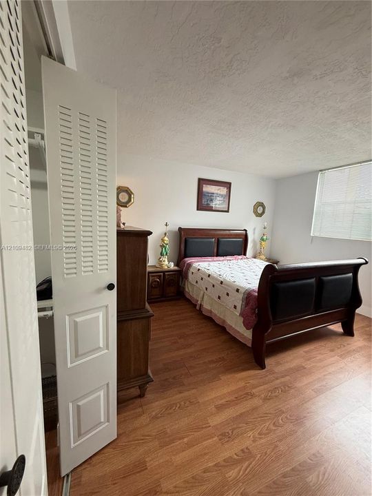 Wood-finish flooring, louvered bi-fold closet door, and a single-pane window with interior blinds