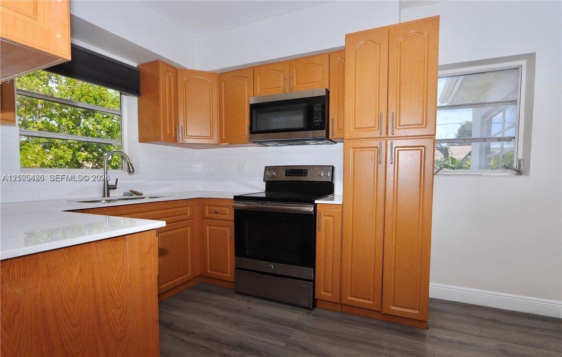 Kitchen featuring wood-finish cabinetry, solid surface countertops, stainless steel appliances, and wood-finish flooring