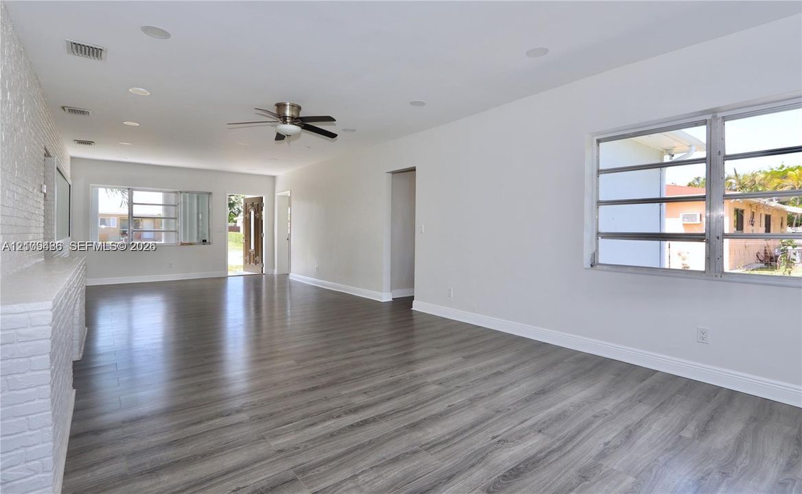 Open living area featuring wood-finish flooring, painted brick accent wall, recessed lighting, ceiling fan, and horizontal louvered windows