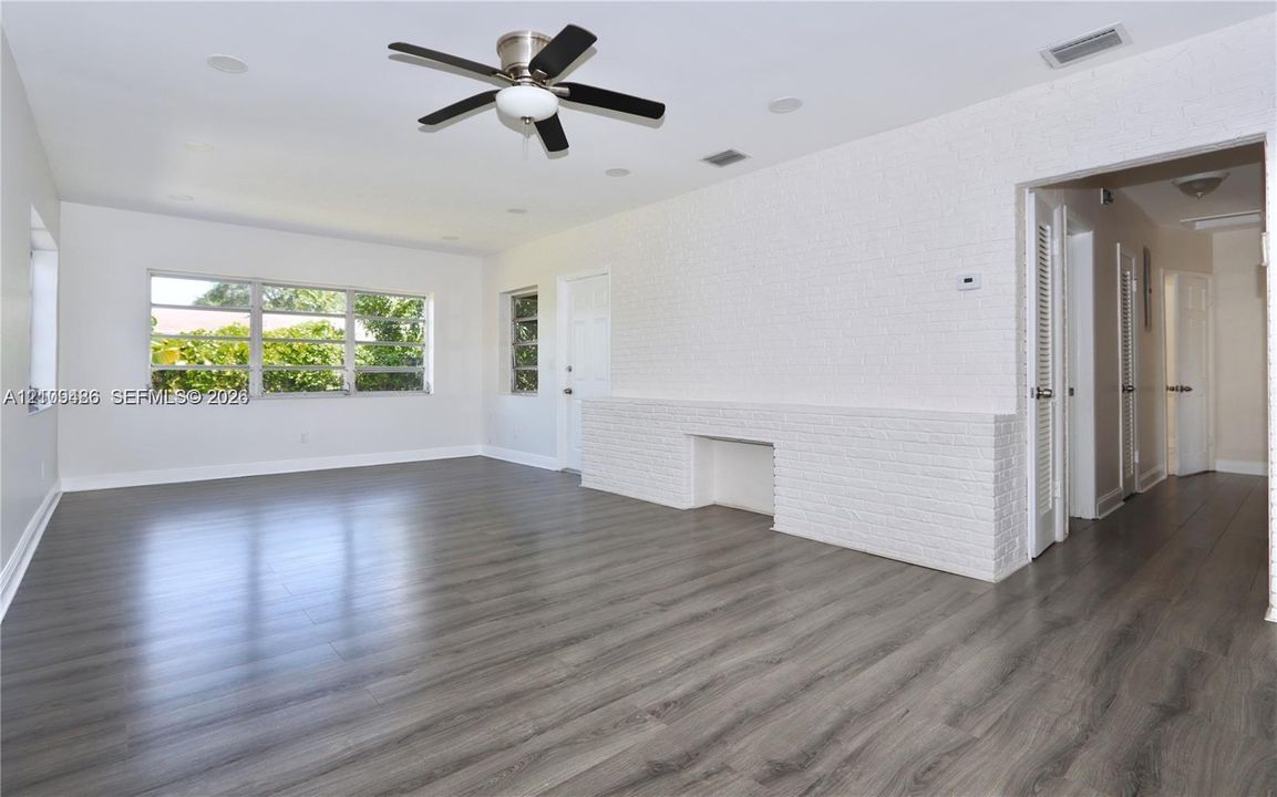Wood-finish flooring, white painted brick architectural detail, multi-pane windows, and a ceiling fan with integrated lighting