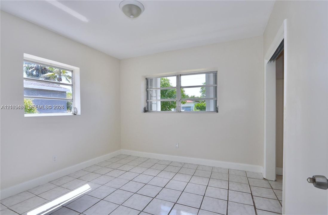 Neutral-toned interior room featuring white tile flooring, two horizontal louvered windows, and a flush-mount ceiling light fixture