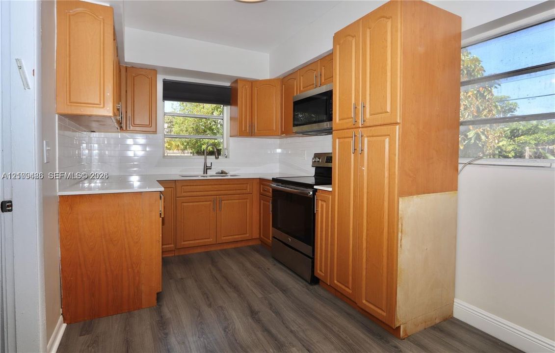 Kitchen featuring wood-finish cabinetry, white countertops, stainless steel appliances, a white tile backsplash, and wood-finish flooring