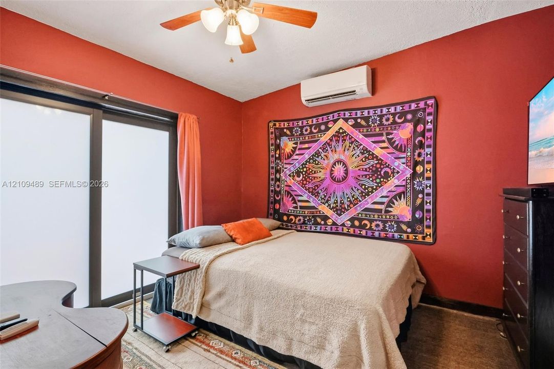 Room featuring a ceiling fan with integrated lighting, wall-mounted ductless air conditioning unit, and sliding glass door