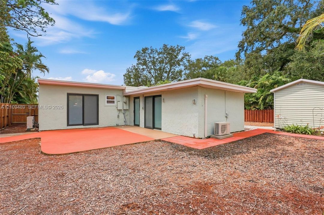 Stucco exterior featuring dual sliding glass doors, a painted concrete patio, and a detached storage structure enclosed by perimeter wood fencing