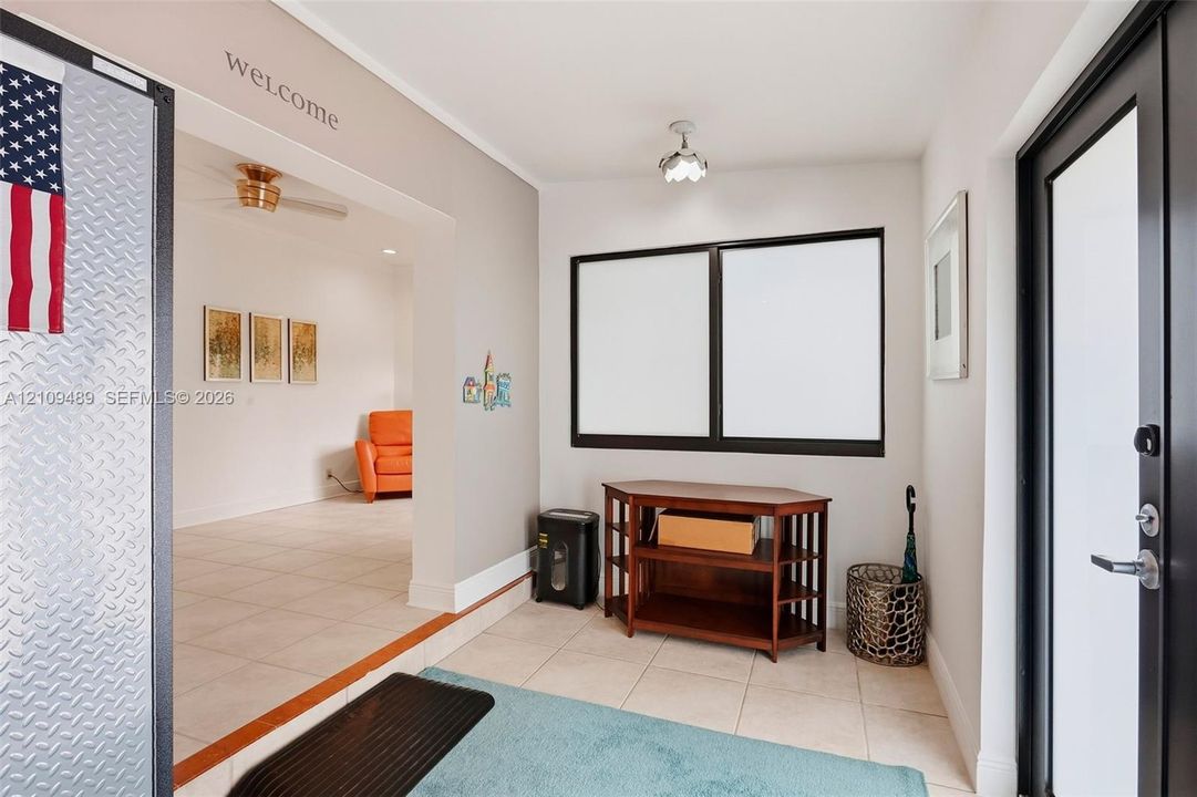 Entryway featuring large-format tile flooring, dual-pane windows with dark frames, and a glass-inset exterior door with metallic hardware