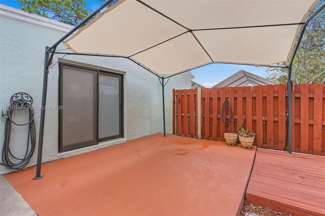Exterior patio featuring a concrete surface, sliding glass door, wooden privacy fencing, and a metal-frame canopy
