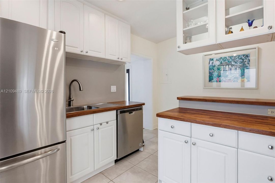 Kitchen featuring white shaker-style cabinetry, wood-finish countertops, stainless steel appliances, a high-arc faucet, and upper glass-front display cabinets