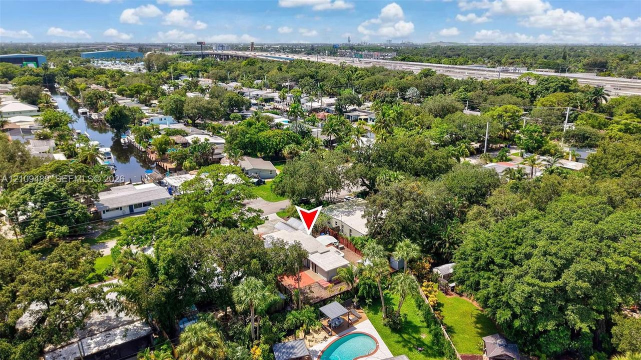 Aerial perspective of a property featuring an in-ground swimming pool, stone-paver pool deck, mature landscaping, and waterfront canal access