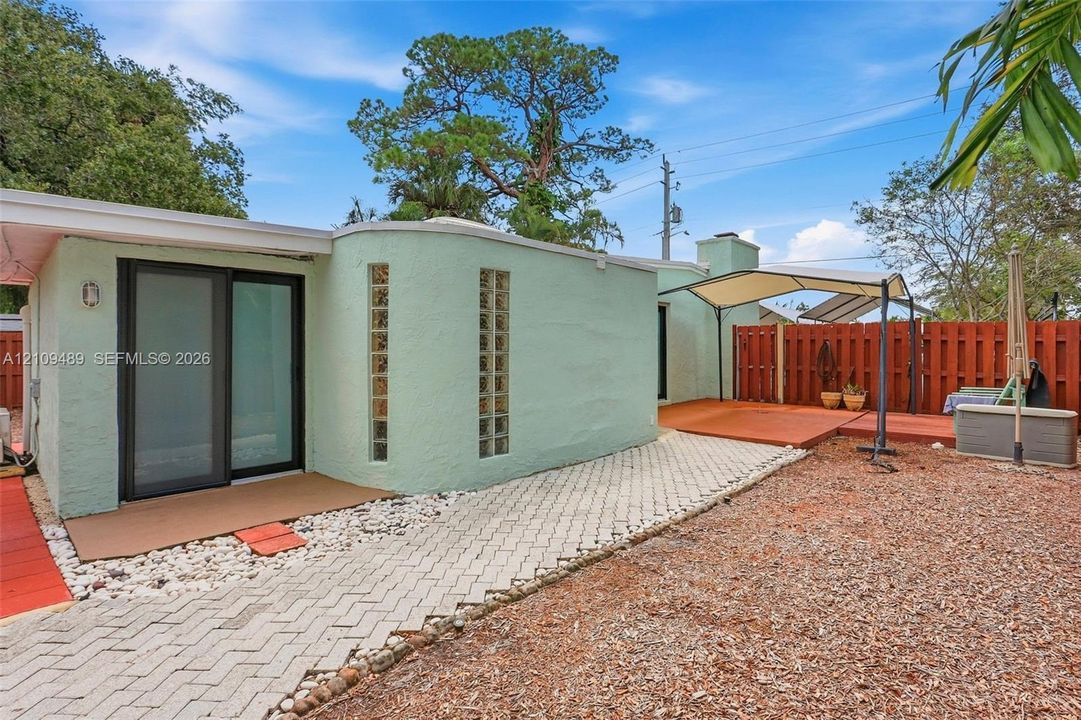 Stucco exterior featuring vertical glass block accents, a sliding glass door, a paved stone pathway, and wood-finish decking