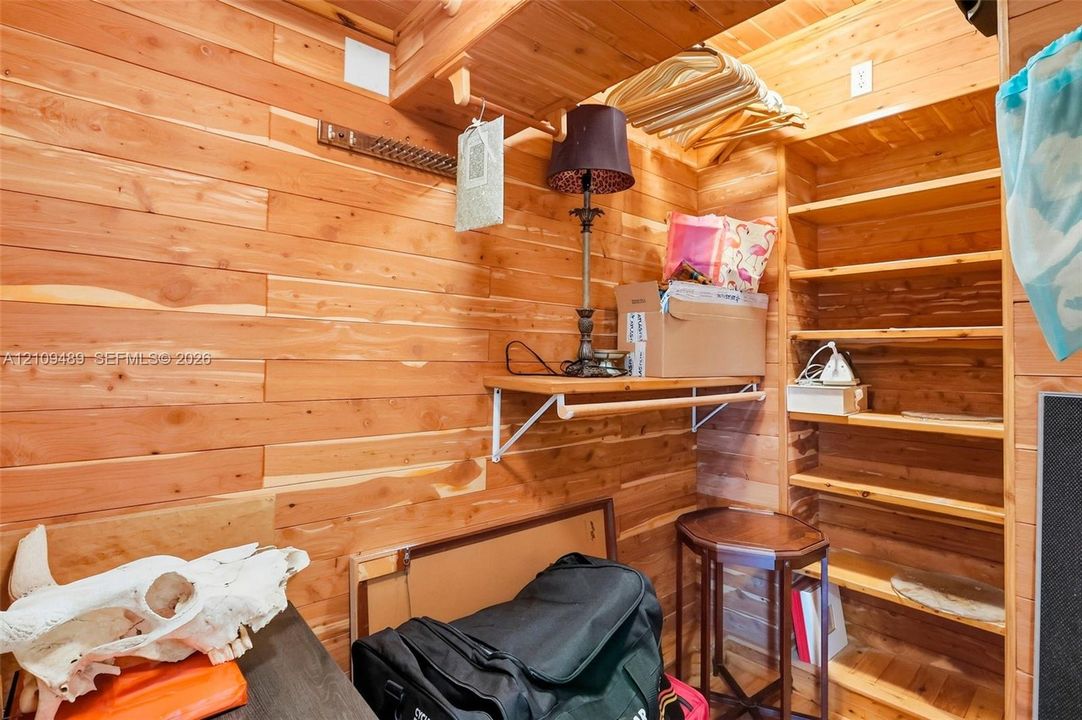 Storage space featuring natural wood-plank wall paneling, built-in wooden shelving, and fixed wooden hanging rods