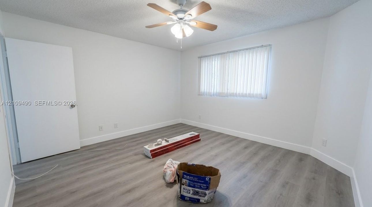 Neutral-toned wood-finish flooring, ceiling fan with integrated lighting, and vertical window blinds