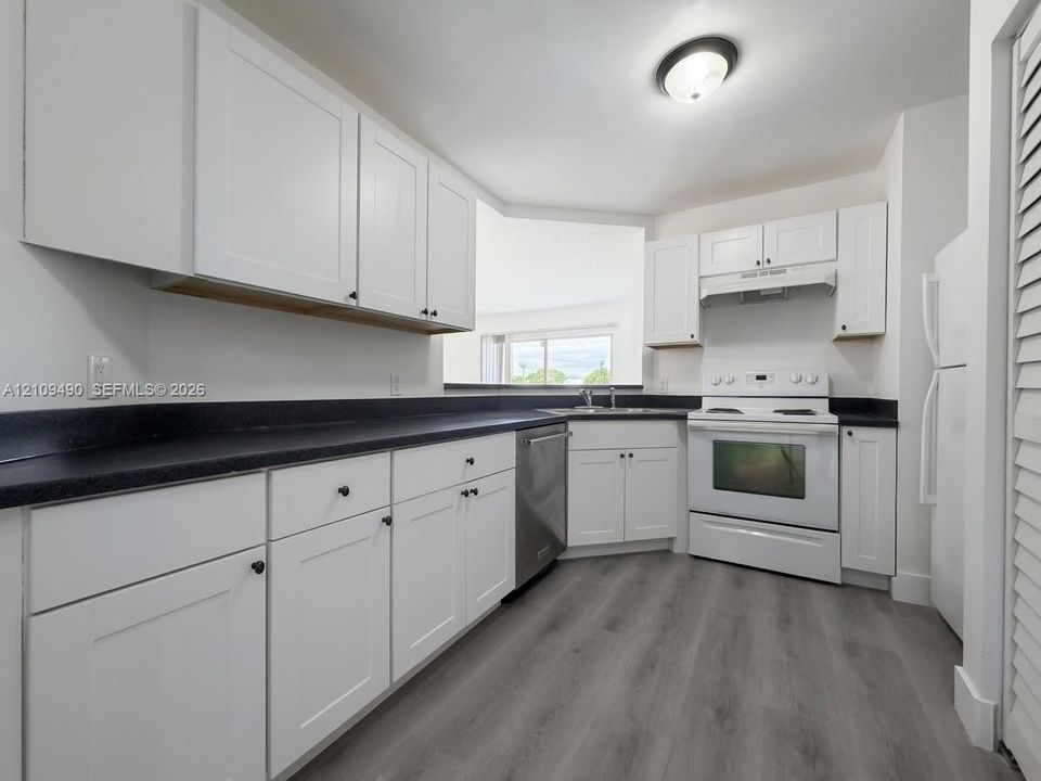 Kitchen featuring white shaker-style cabinetry, dark stone-finish countertops, wood-finish flooring, and stainless steel dishwasher