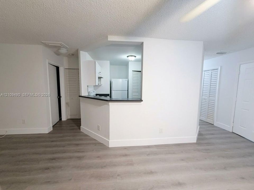 Kitchen pass-through window with a breakfast bar, wood-finish flooring, white cabinetry, and louvered closet doors