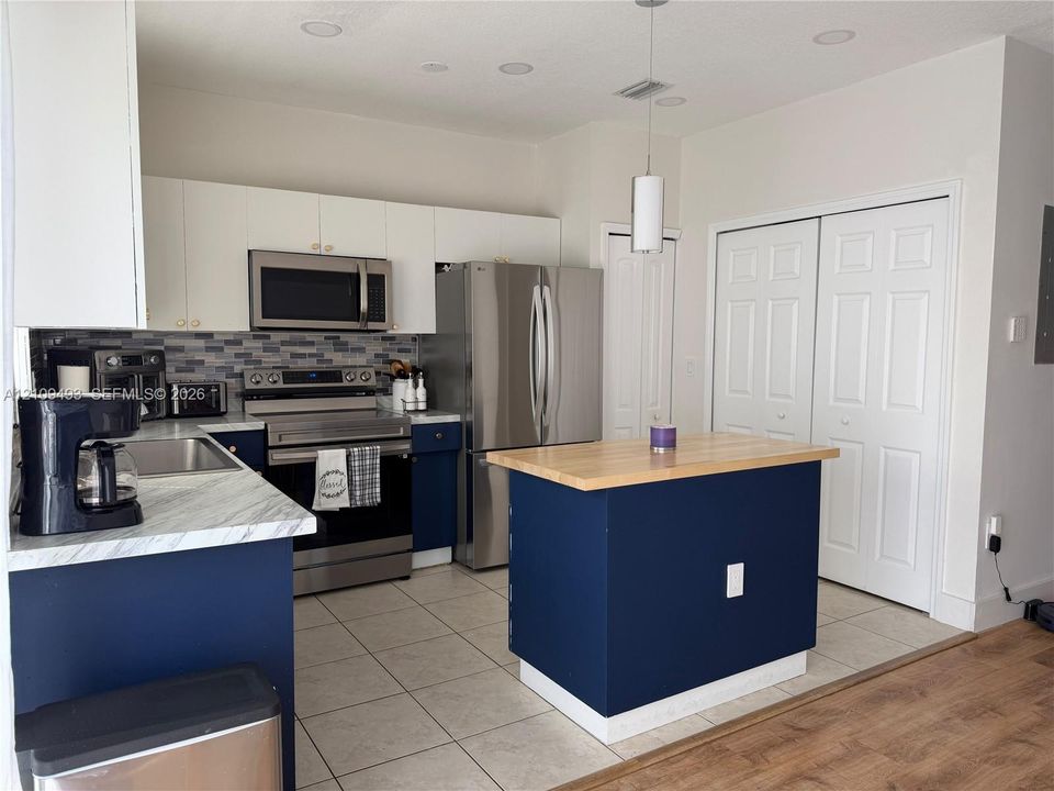 Kitchen featuring a center island with a wood-finish countertop, dual-tone cabinetry, stainless steel appliances, a multi-tone tile backsplash, and recessed lighting