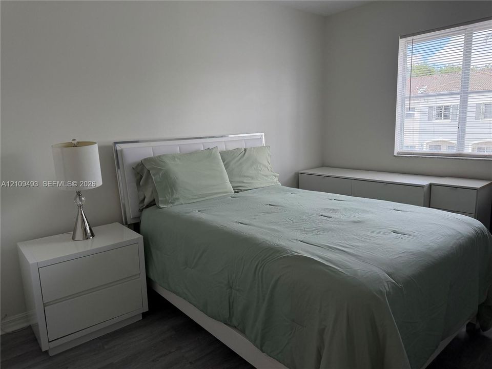 Neutral interior space featuring wood-finish flooring and a single-pane window with horizontal blinds