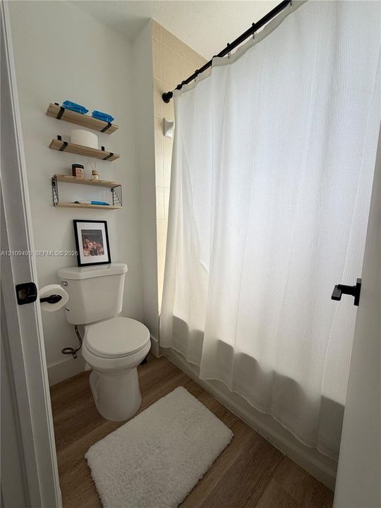 Bathroom featuring wood-finish flooring, a combination tub and shower with tile surround, and matte black hardware
