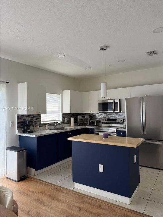Kitchen featuring two-tone cabinetry, stainless steel appliances, a wood-top center island, and mosaic tile backsplash
