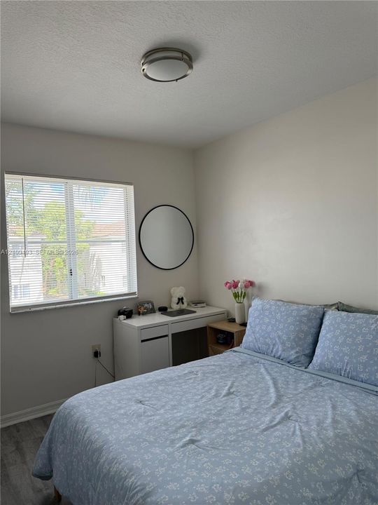 Neutral-toned interior featuring wood-finish flooring, a large window, and a circular wall-mounted mirror