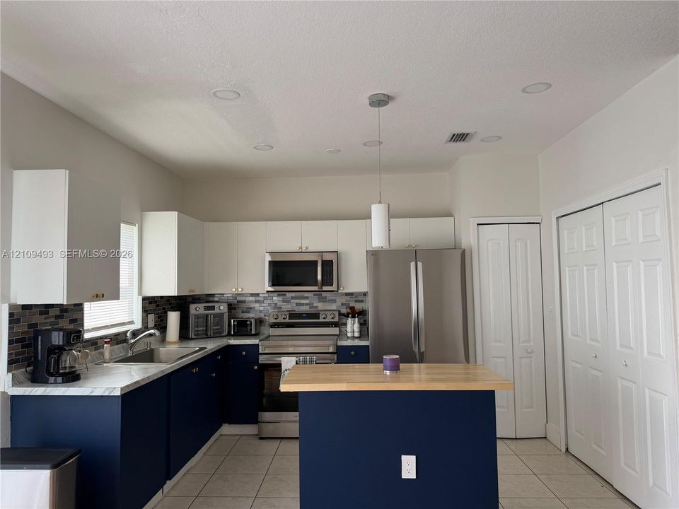 Kitchen featuring two-tone cabinetry, stainless steel appliances, a wood-top island, mosaic tile backsplash, and recessed lighting
