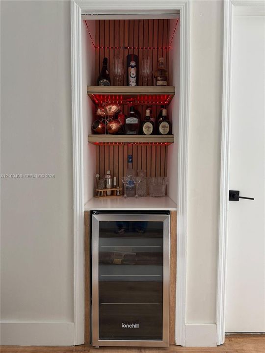 Built-in wall niche featuring vertical wood slat paneling, custom shelving, stone countertop, and integrated under-cabinet lighting