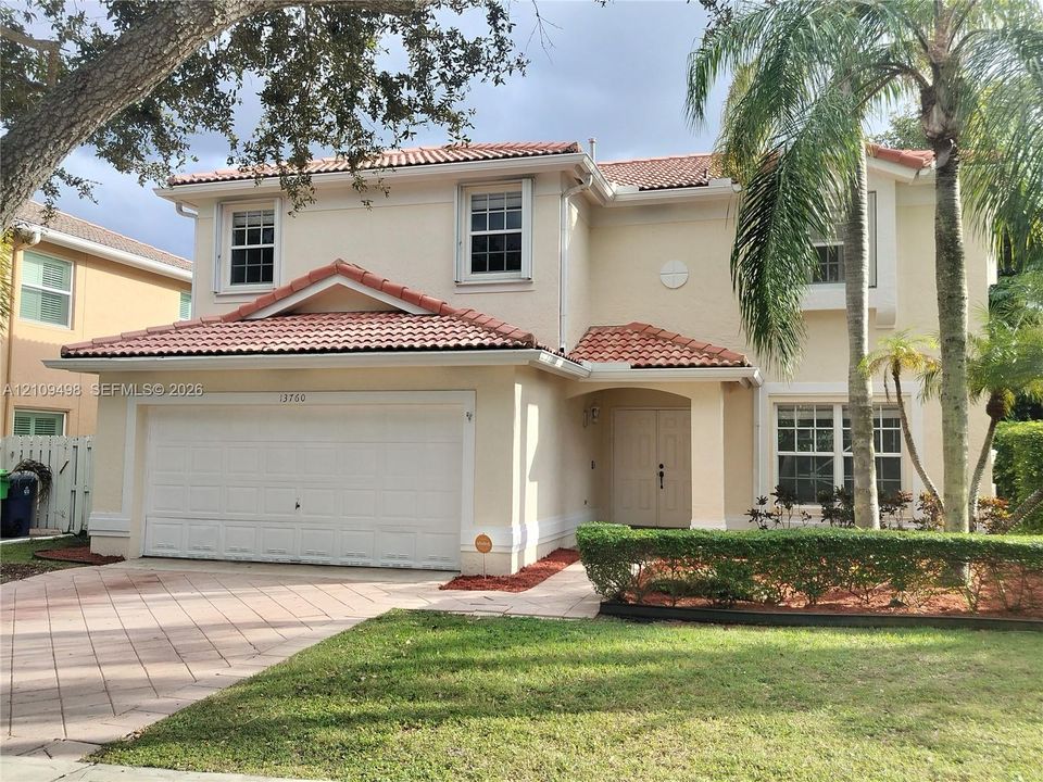 Two-story exterior featuring a stucco facade, red tile roofing, a paved driveway, and double-door entryway
