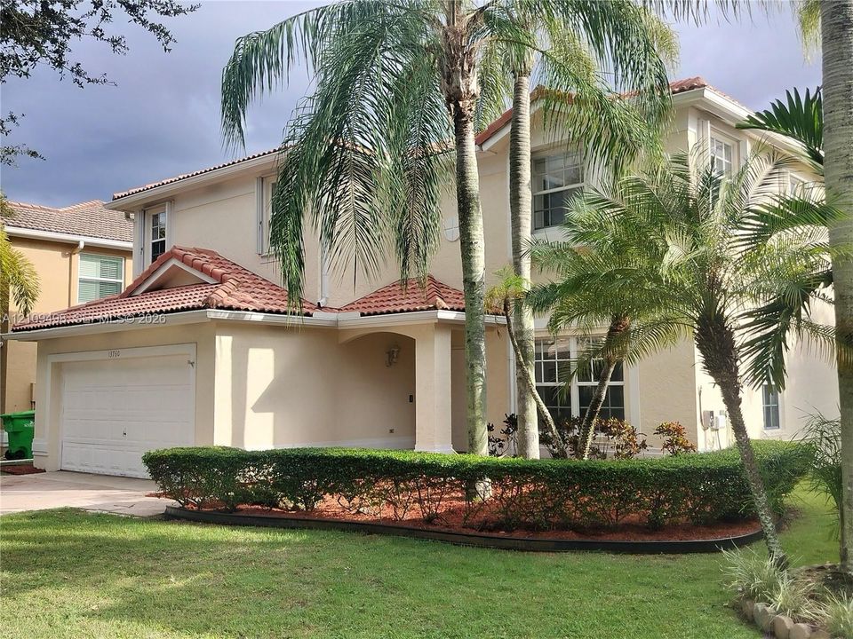 Two-story exterior featuring a clay tile roof, multi-paned windows, a covered entryway, and a multi-car garage
