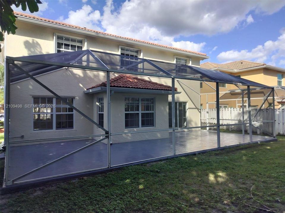 Screen-enclosed rear patio featuring a concrete floor, stucco exterior, multi-pane windows, and a tile roof