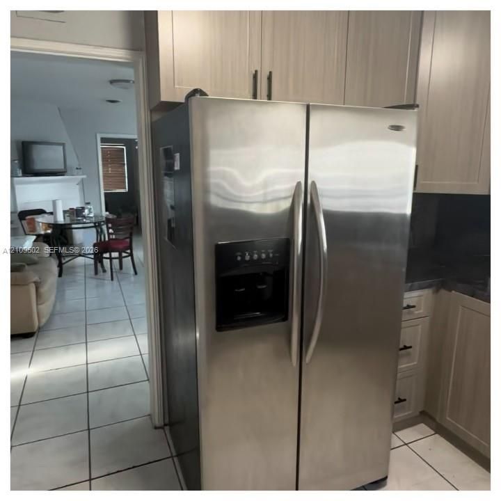 Stainless steel side-by-side refrigerator, light-toned cabinetry with modern hardware, and neutral ceramic tile flooring