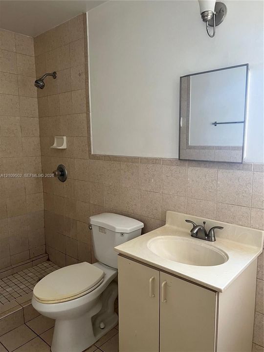 Bathroom featuring tiled walls, a shower stall, a vanity cabinet with an integrated sink, a dual-handle faucet, and a wall-mounted medicine cabinet