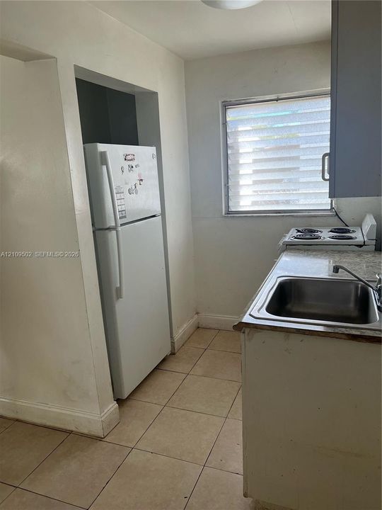 Kitchen featuring ceramic tile flooring, stone-finish countertops, stainless steel sink with metal faucet, and built-in cabinetry