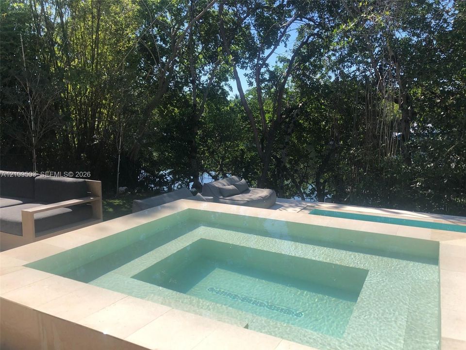 In-ground pool and integrated spa featuring stone coping and surrounding mature trees