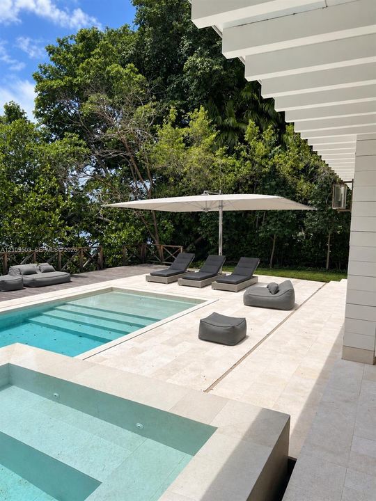 Outdoor space featuring a swimming pool with integrated spa, light-toned stone decking, wood-finish perimeter fencing, and a white pergola structure