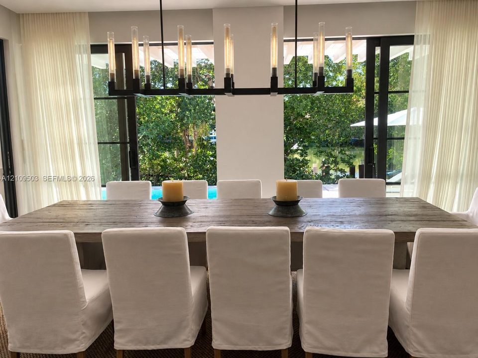 Linear wrought iron chandelier with exposed filament bulbs, floor-to-ceiling metal-framed glass doors, and direct outdoor access