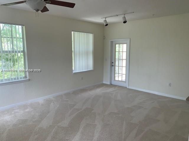 Neutral interior space featuring carpeting, a multi-light ceiling fan, adjustable track lighting, and a glass-paned exterior door