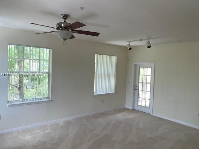 Neutral wall tones, carpeting, ceiling fan with light fixture, adjustable track lighting, and exterior glass-panel door