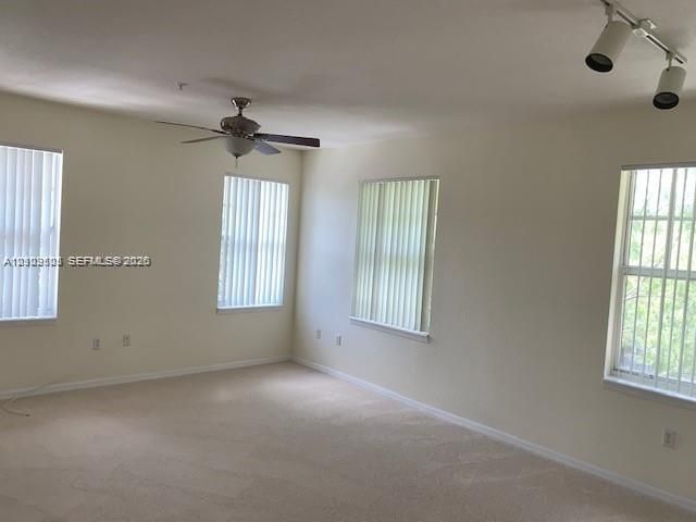 Neutral interior featuring neutral wall-to-wall carpeting, multiple windows with vertical blinds, a ceiling fan, and track lighting