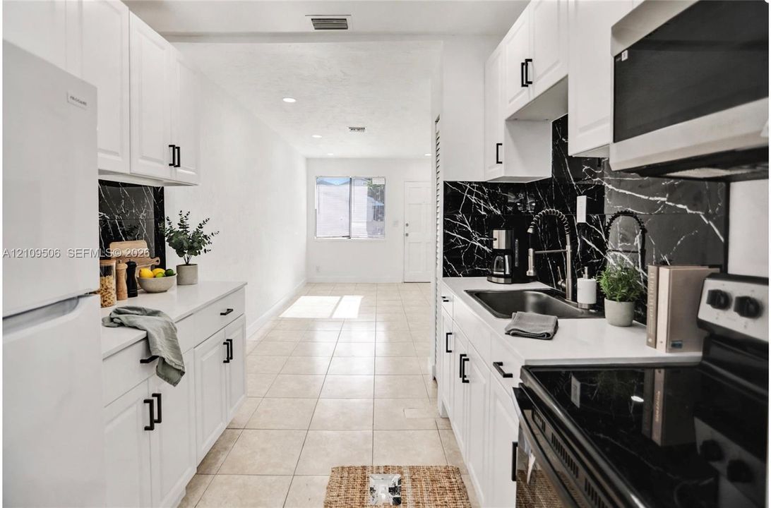 Kitchen featuring white shaker-style cabinetry, solid-surface countertops, high-contrast dark stone-patterned backsplash, undermount sink with arched pull-down faucet, and recessed lighting