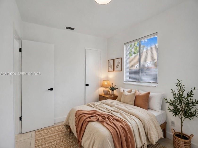 Staged interior featuring white walls, tile flooring, two solid-core doors with matte black hardware, and a single-pane window with horizontal blinds