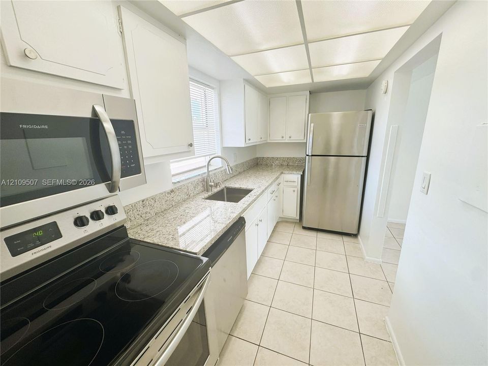 Kitchen featuring stone countertops, stainless steel refrigerator, over-the-range microwave, white cabinetry, and tile flooring