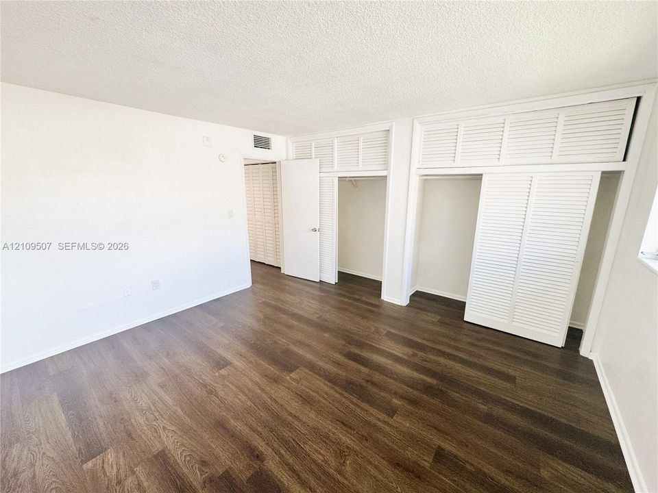Wood-finish flooring throughout, featuring expansive floor-to-ceiling closets with white louvered doors and overhead storage compartments