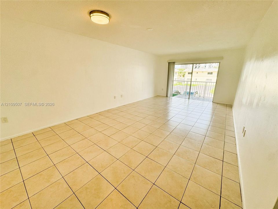 Neutral-toned tile flooring, flush-mount ceiling light fixture, and sliding glass doors leading to an exterior balcony