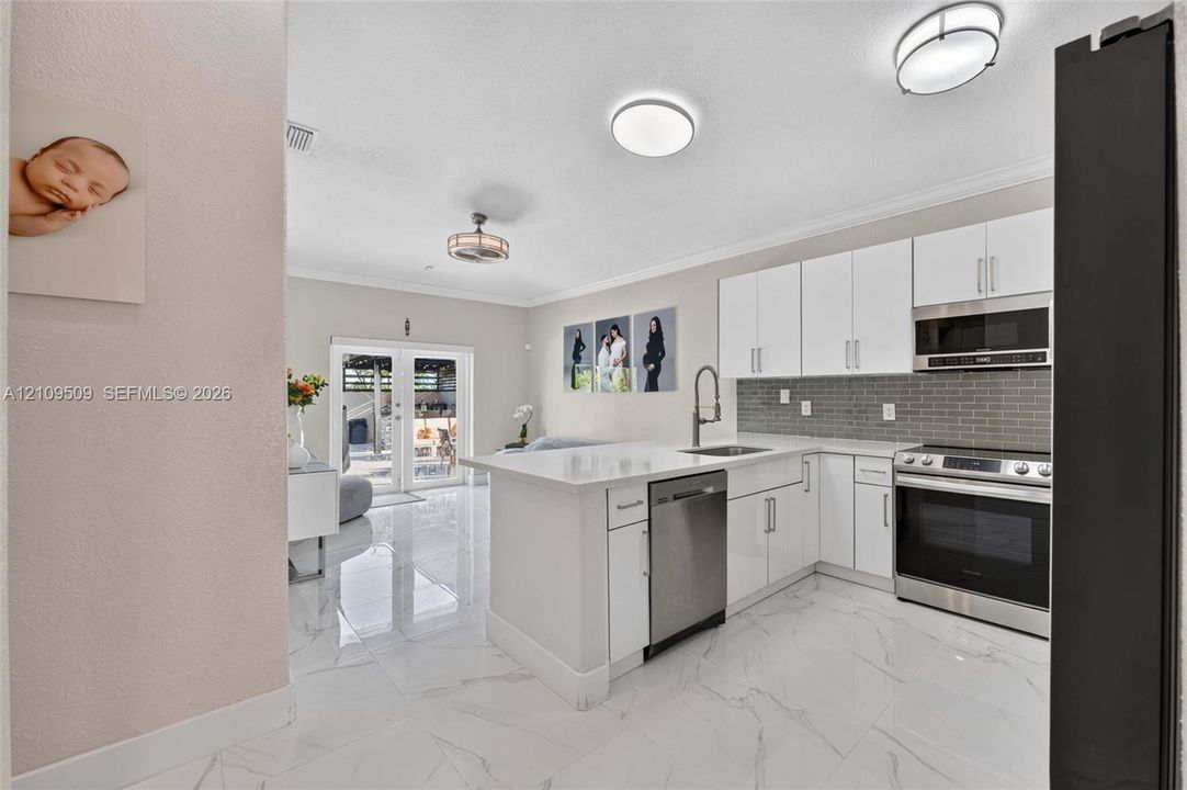Kitchen featuring flat-panel white cabinetry, stone-finish countertops, stainless steel appliances, a grey subway tile backsplash, and polished tile flooring