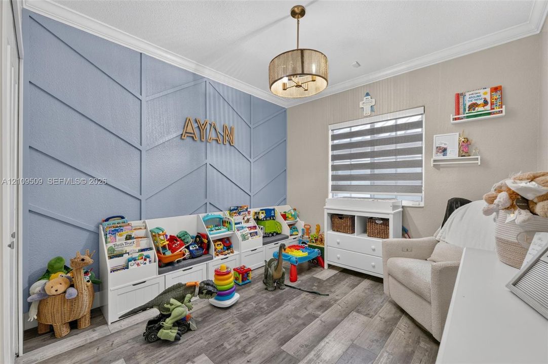 Accent wall with decorative geometric molding, wood-finish flooring, crown molding, drum pendant light fixture, and horizontal window shades