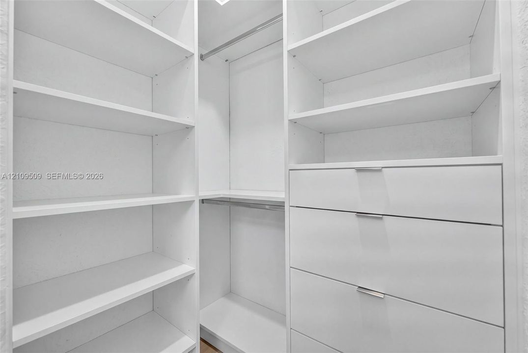 Custom built-in storage featuring white cabinetry, multiple open shelving units, integrated clothing rods, and soft-close drawers with minimalist hardware