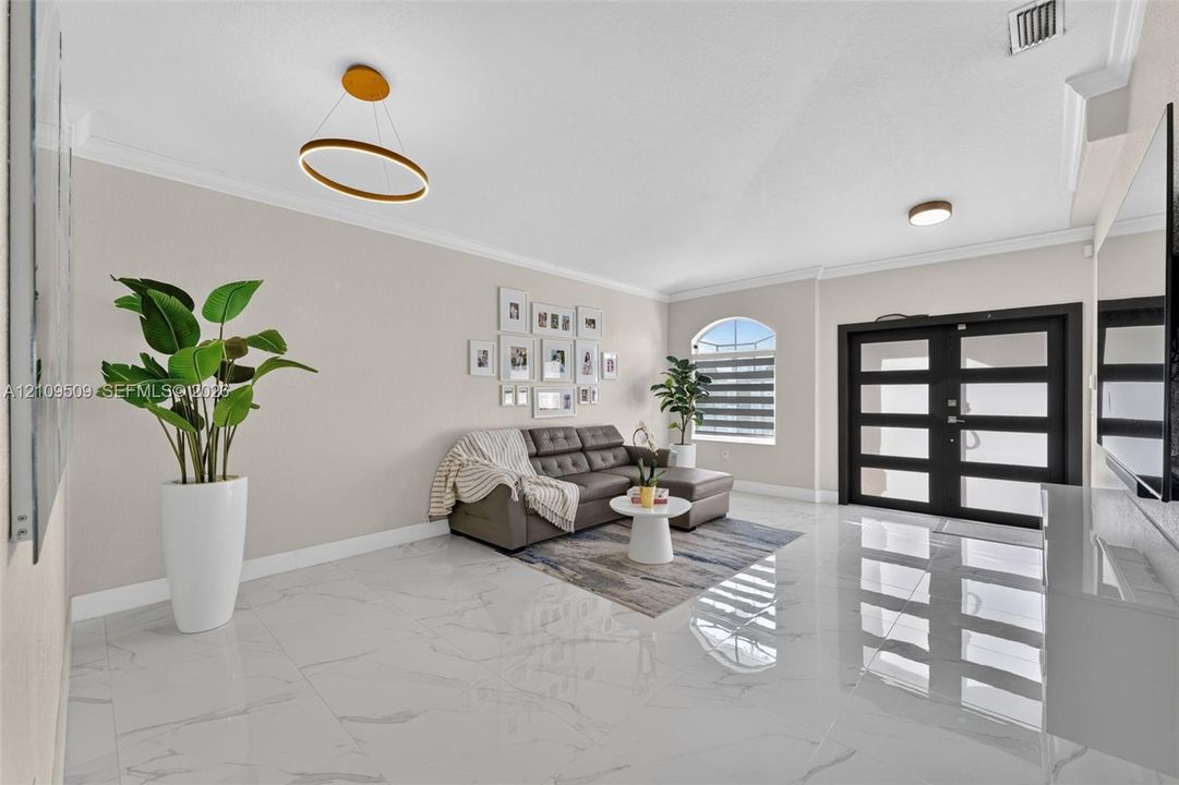 Large-format polished tile flooring, double-door entry with glass panels, crown molding, modern ring-style pendant lighting, and an arched window