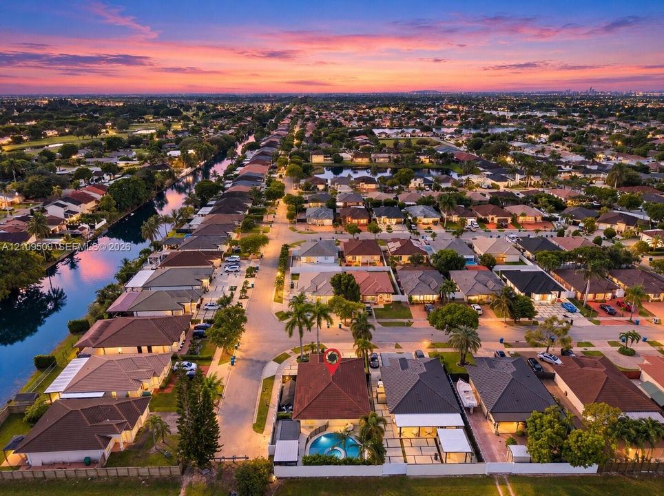 Aerial perspective of a residential property featuring a tiled roof, an in-ground swimming pool, a stone-paver patio, and mature palm trees