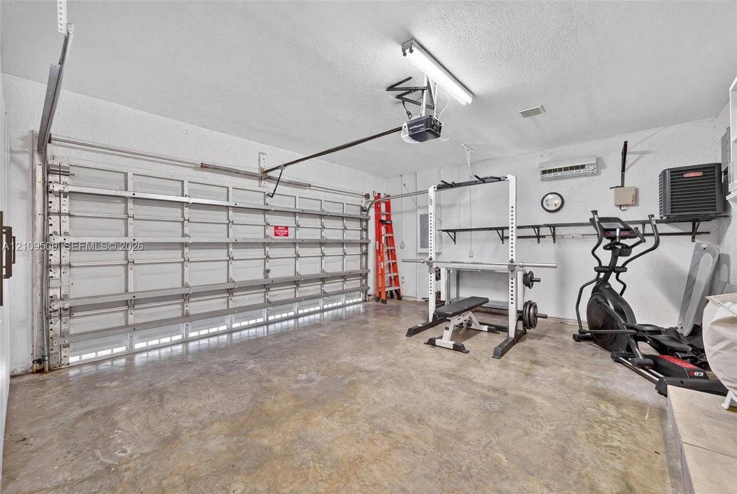 Multi-car garage featuring a concrete floor, motorized sectional garage door, wall-mounted ductless mini-split system, and built-in wall shelving