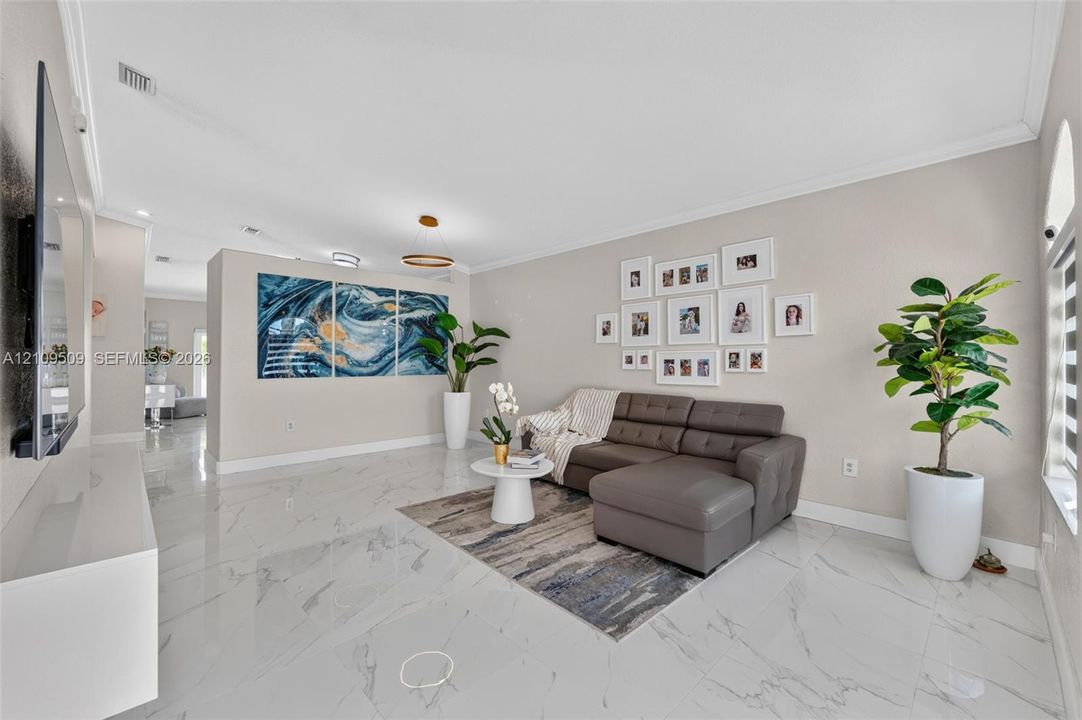 Open floor plan living area featuring polished stone-finish floor tiling, crown molding, recessed lighting, and a modern tiered pendant light fixture
