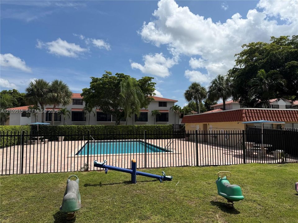 Outdoor swimming pool enclosed by metal fencing, featuring a paver deck, mature palm trees, and manicured lawn